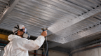 Worker spraying radiant barrier paint onto reflective foil-like ceiling panels